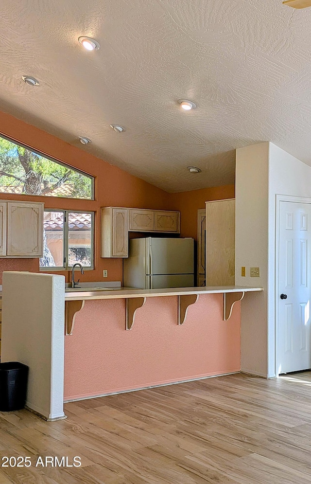 kitchen featuring freestanding refrigerator, a breakfast bar, a textured ceiling, light wood-style flooring, and lofted ceiling