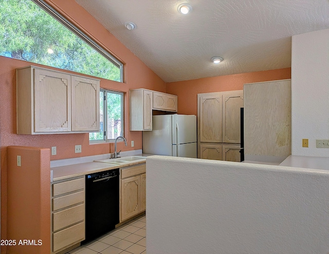 kitchen with black dishwasher, freestanding refrigerator, a sink, light countertops, and vaulted ceiling