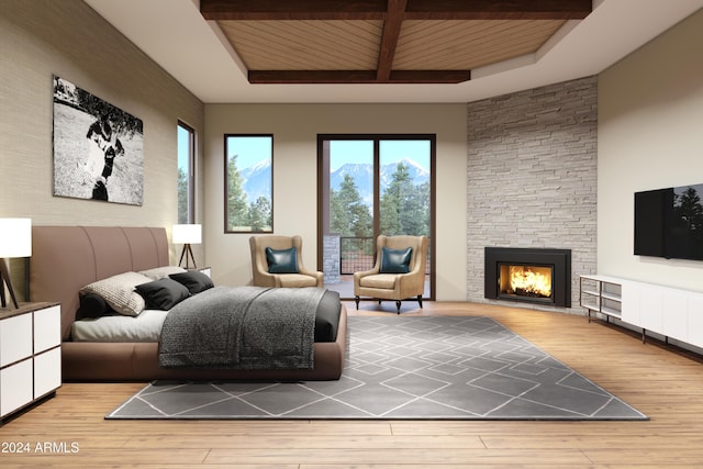 bedroom with beamed ceiling, a stone fireplace, and wood finished floors