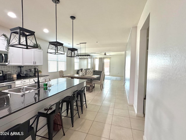 kitchen featuring appliances with stainless steel finishes, light tile patterned flooring, white cabinetry, a breakfast bar area, and decorative light fixtures