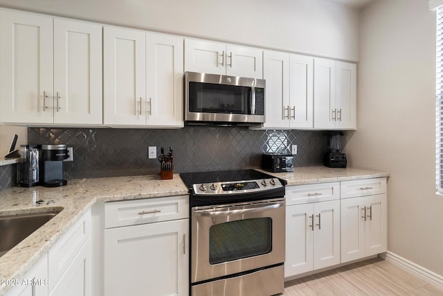 kitchen featuring light wood-style flooring, white cabinetry, appliances with stainless steel finishes, decorative backsplash, and light stone countertops