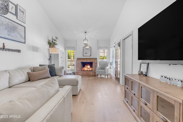 living area with high vaulted ceiling, light wood finished floors, and a tiled fireplace