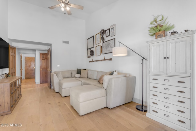 living area with ceiling fan, a high ceiling, light wood-style floors, and visible vents