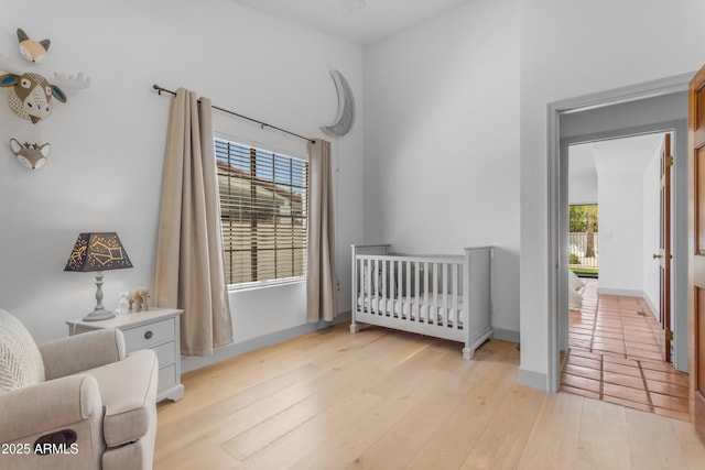 bedroom with baseboards, a crib, and light wood-style flooring