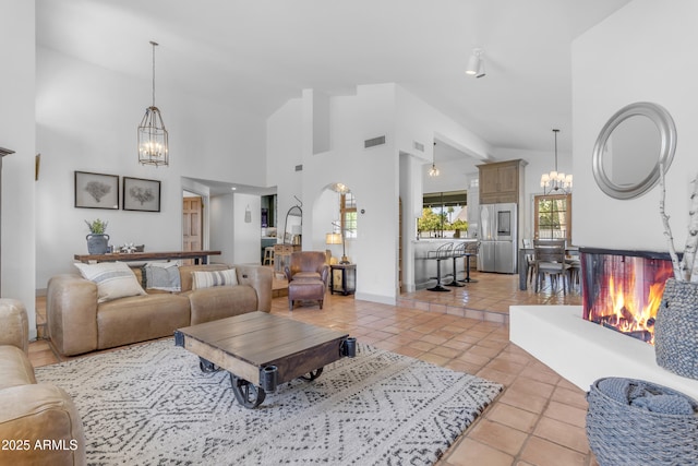 living room featuring high vaulted ceiling, light tile patterned floors, baseboards, a notable chandelier, and visible vents