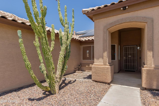 16288 W Hadley St, Goodyear, AZ 85338 - view of exterior entry with a tile roof, solar panels, and stucco siding