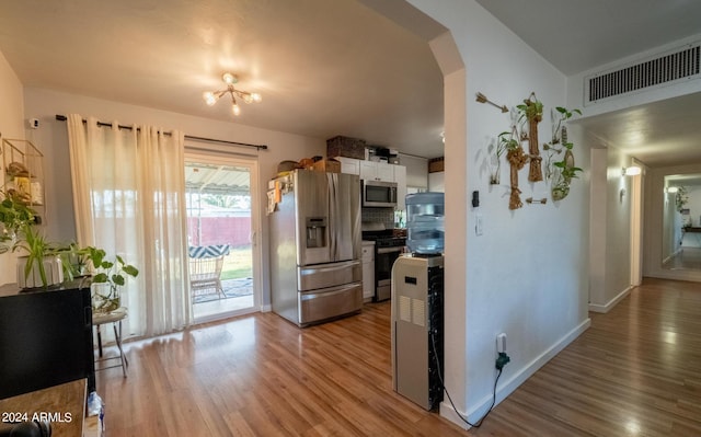 kitchen featuring white cabinets, tasteful backsplash, stainless steel appliances, an inviting chandelier, and light wood-type flooring