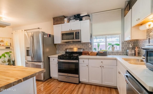 kitchen with appliances with stainless steel finishes, light hardwood / wood-style floors, white cabinetry, and tasteful backsplash