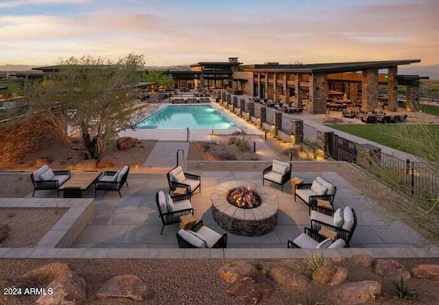 pool at dusk featuring a patio and an outdoor living space with a fire pit