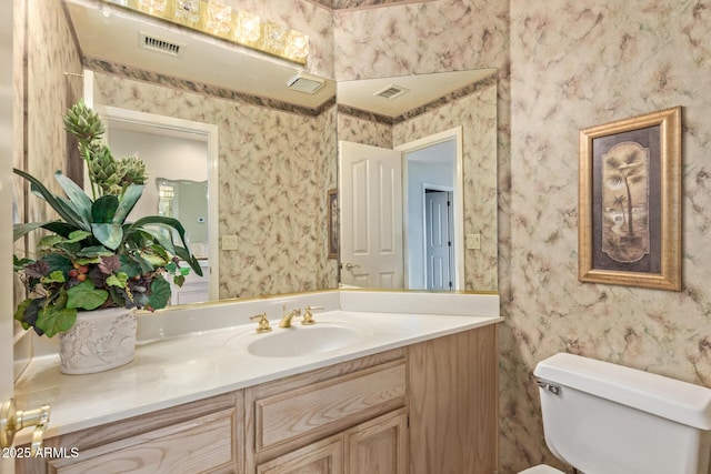 bathroom featuring visible vents, toilet, vanity, and wallpapered walls