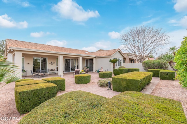 rear view of property featuring stucco siding, fence, a patio area, a yard, and a tiled roof