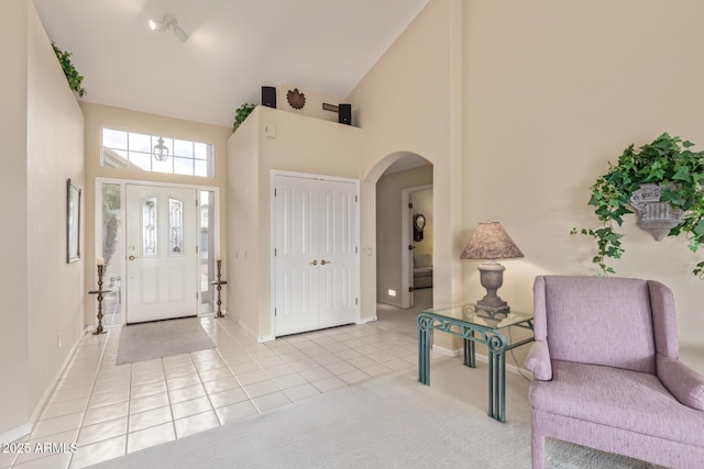 foyer with light tile patterned floors, baseboards, high vaulted ceiling, arched walkways, and light carpet