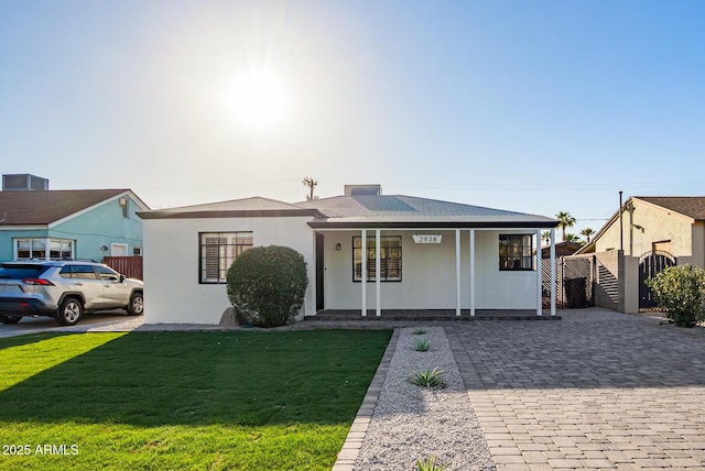 ranch-style home featuring stucco siding, decorative driveway, covered porch, a front yard, and central AC unit