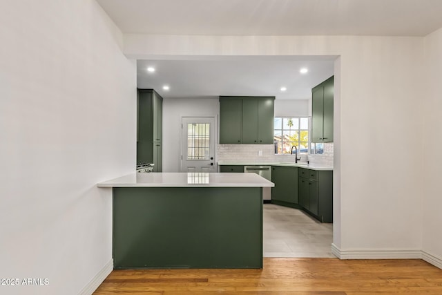 kitchen with a peninsula, stainless steel dishwasher, light countertops, green cabinets, and backsplash