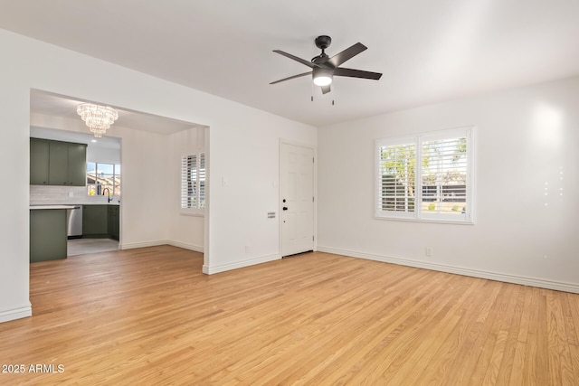 empty room with plenty of natural light, ceiling fan with notable chandelier, baseboards, and light wood-style floors