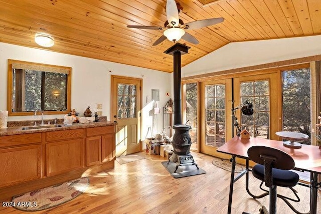 dining area with a wood stove, sink, light hardwood / wood-style flooring, vaulted ceiling, and wood ceiling