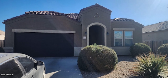 mediterranean / spanish-style home featuring a tile roof, concrete driveway, stucco siding, fence, and an attached garage