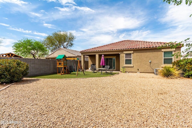 rear view of property featuring stucco siding, a fenced backyard, a tiled roof, a playground, and a lawn