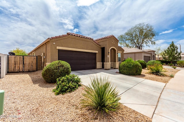 mediterranean / spanish-style home featuring a tile roof, concrete driveway, stucco siding, a gate, and a garage
