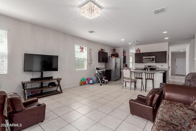 living room featuring light tile patterned flooring, visible vents, a healthy amount of sunlight, and an inviting chandelier