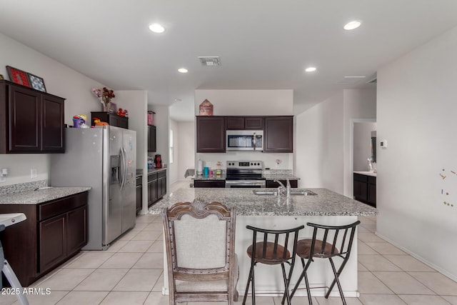 kitchen with light tile patterned floors, stainless steel appliances, a sink, an island with sink, and visible vents