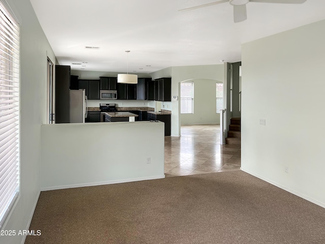 kitchen featuring dark cabinetry, visible vents, ceiling fan, stainless steel appliances, and light carpet