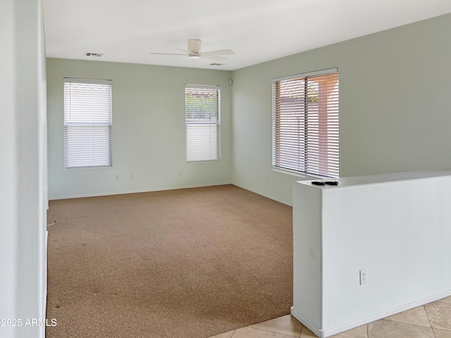 unfurnished room featuring visible vents, baseboards, light colored carpet, light tile patterned floors, and a ceiling fan