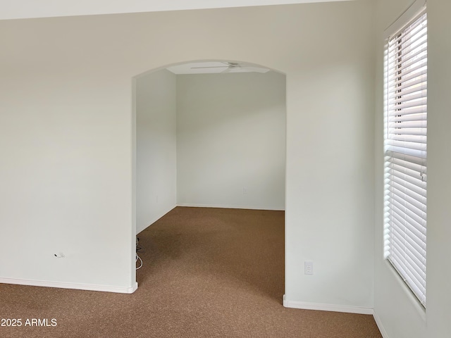 carpeted spare room featuring baseboards and arched walkways