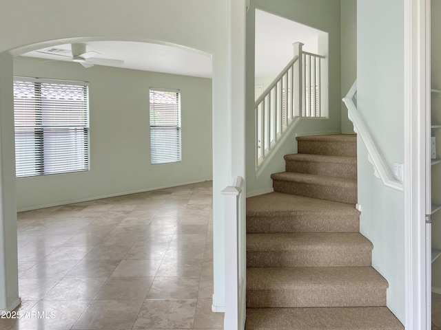 staircase with arched walkways, tile patterned flooring, baseboards, and a ceiling fan