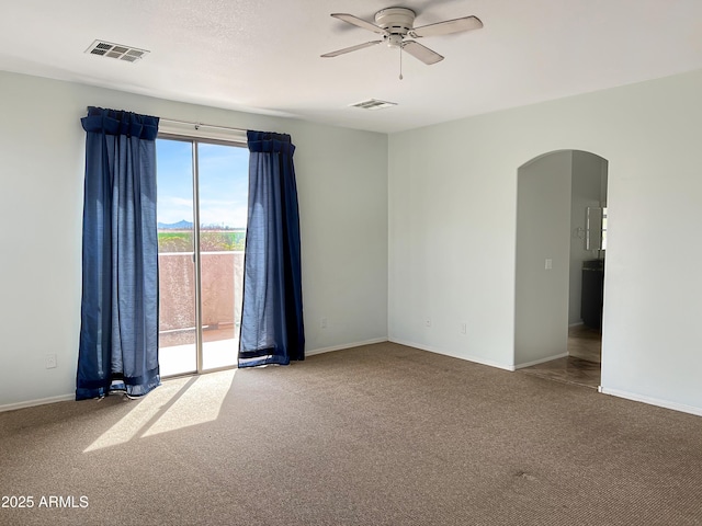 carpeted spare room featuring visible vents, arched walkways, baseboards, and a ceiling fan