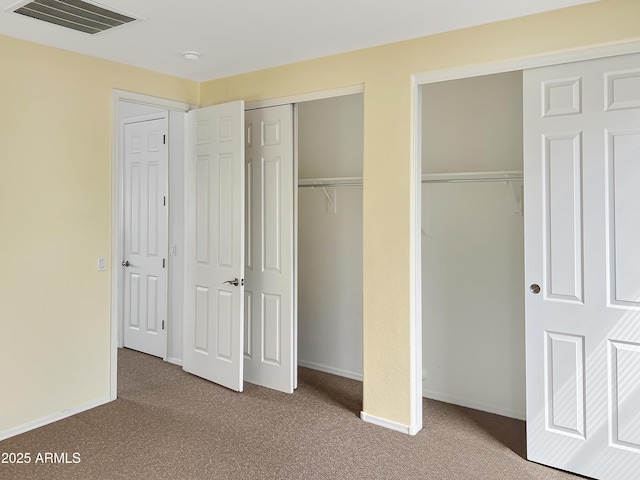 unfurnished bedroom with visible vents, baseboards, two closets, and carpet floors