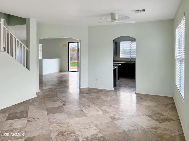 unfurnished room with arched walkways, visible vents, baseboards, and ceiling fan