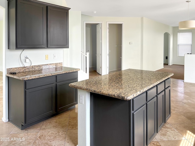 kitchen featuring arched walkways, open floor plan, stone countertops, and a center island