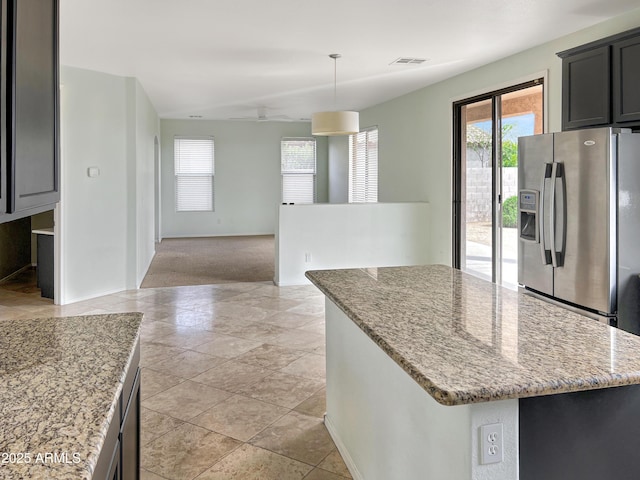 kitchen featuring visible vents, light stone counters, decorative light fixtures, a center island, and stainless steel fridge