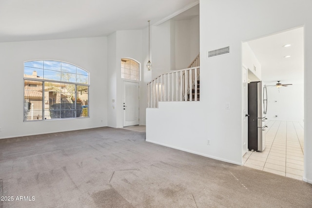 unfurnished living room with visible vents, light colored carpet, ceiling fan, stairs, and high vaulted ceiling