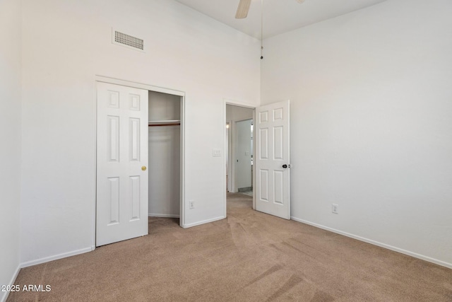 unfurnished bedroom featuring baseboards, visible vents, light colored carpet, a high ceiling, and a closet