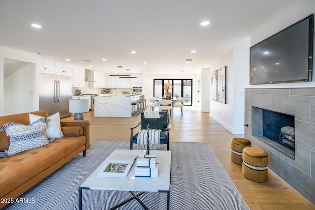 living room with a tiled fireplace, sink, and light wood-type flooring