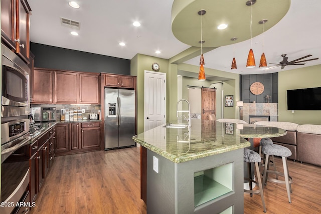 kitchen with hanging light fixtures, a barn door, appliances with stainless steel finishes, open floor plan, and a sink