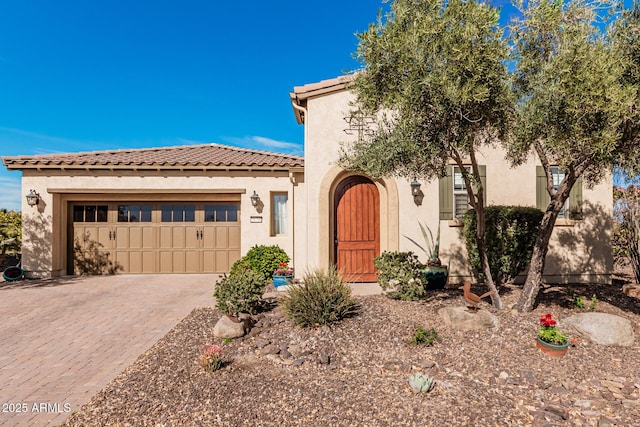 mediterranean / spanish-style house with an attached garage, a tile roof, decorative driveway, and stucco siding