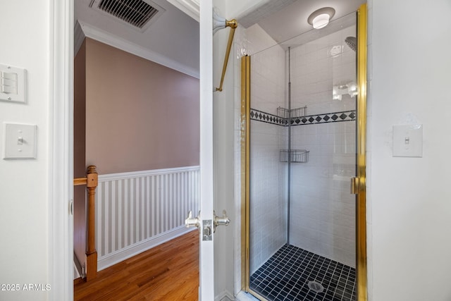 full bathroom with a wainscoted wall, wood finished floors, visible vents, ornamental molding, and a stall shower