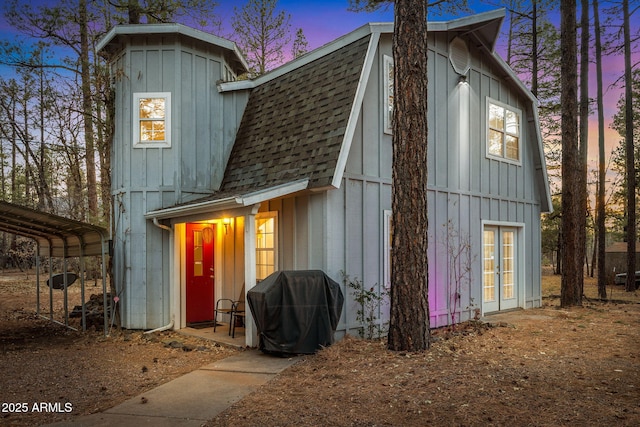 back of house at dusk with a detached carport, a shingled roof, board and batten siding, and a gambrel roof