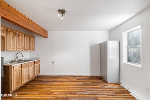 kitchen with wood finished floors, a sink, baseboards, light countertops, and beam ceiling