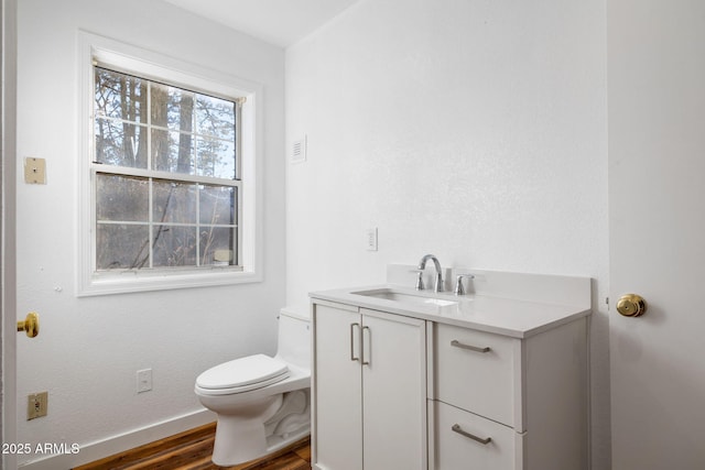 half bathroom with baseboards, vanity, toilet, and wood finished floors