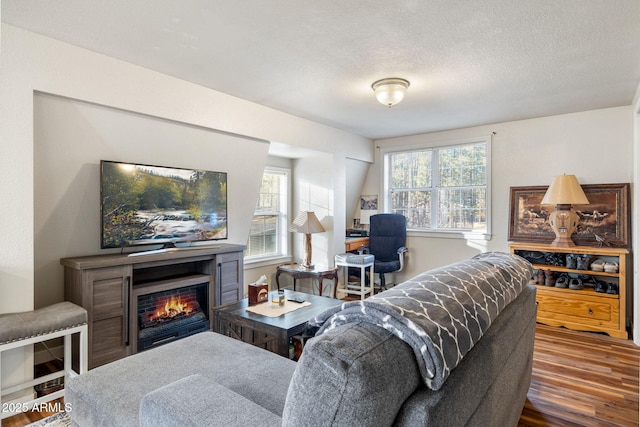 living area with a lit fireplace, a textured ceiling, and wood finished floors