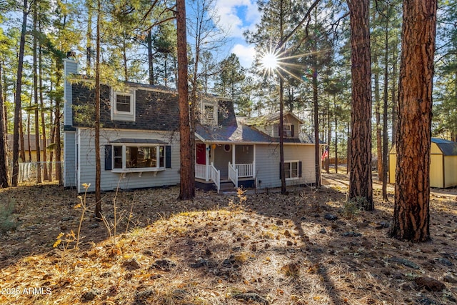 view of front of home with a chimney, a storage unit, a shingled roof, fence, and an outdoor structure