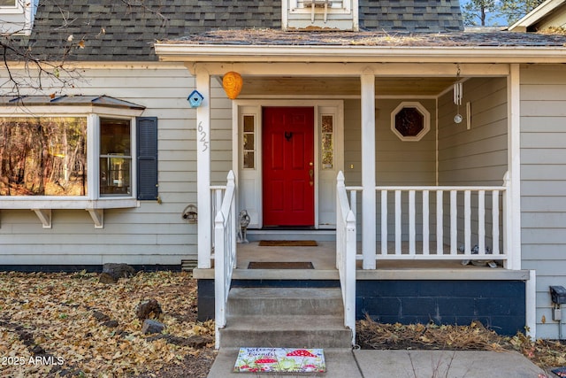 entrance to property featuring covered porch and roof with shingles