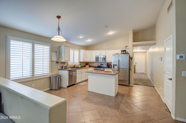 kitchen featuring appliances with stainless steel finishes, decorative light fixtures, white cabinetry, a kitchen island, and lofted ceiling