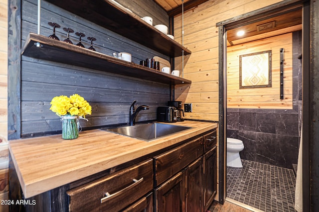 kitchen with wood walls, sink, butcher block counters, dark brown cabinetry, and tile patterned floors