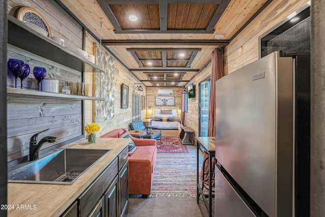 kitchen with sink, wood counters, wooden ceiling, wooden walls, and stainless steel fridge