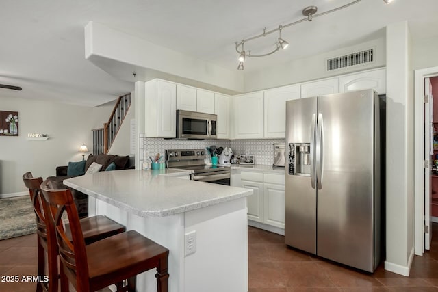 kitchen featuring visible vents, decorative backsplash, appliances with stainless steel finishes, a peninsula, and white cabinetry